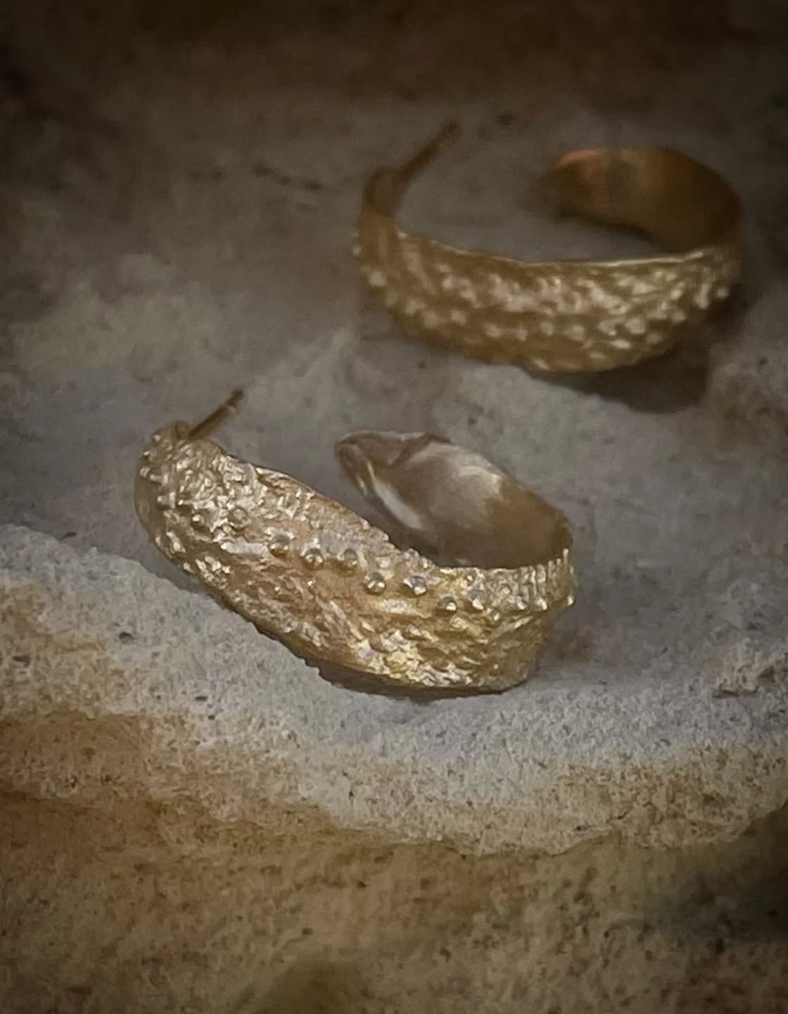 Kreolernes tekstur får mig til at tænke på et korallrevs porøse overflade, eroderet af århundreders bølgeslag. De tætsiddende knopper og uregelmæssige fordybninger skaber et relief, der genskinner som dråber på en grusvej, regnen netop har forladt. Smykket gengiver den uforfalskede skønhed, der findes, når materialer får lov til at tale deres eget sprog. 🕊️
Find kreolerne i butikken og på webshoppen under navnet "Angitia" ✨