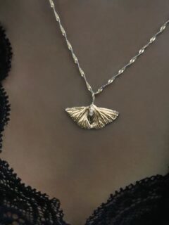 FALENA
Natsværmerens vinger er brede og detaljerede, fanget i et øjebliks ro midt i dens evige søgen efter lys ✨
Dens overflade reflekterer aftenens sidste stråler med en varm, dyb glød – som om den har badet i tusmørkets gyldne timer og båret dets skær med sig.

I midten udgør tre små topassten smykkets balancepunkt.
Kæden er en tæt tvillingespiral, der snor sig opad mod halsens kurve. I sin helhed er smykket en stum påmindelse om, at skønheden ofte findes i det flygtige ✨

Halskæden fås også i sterlingsølv.